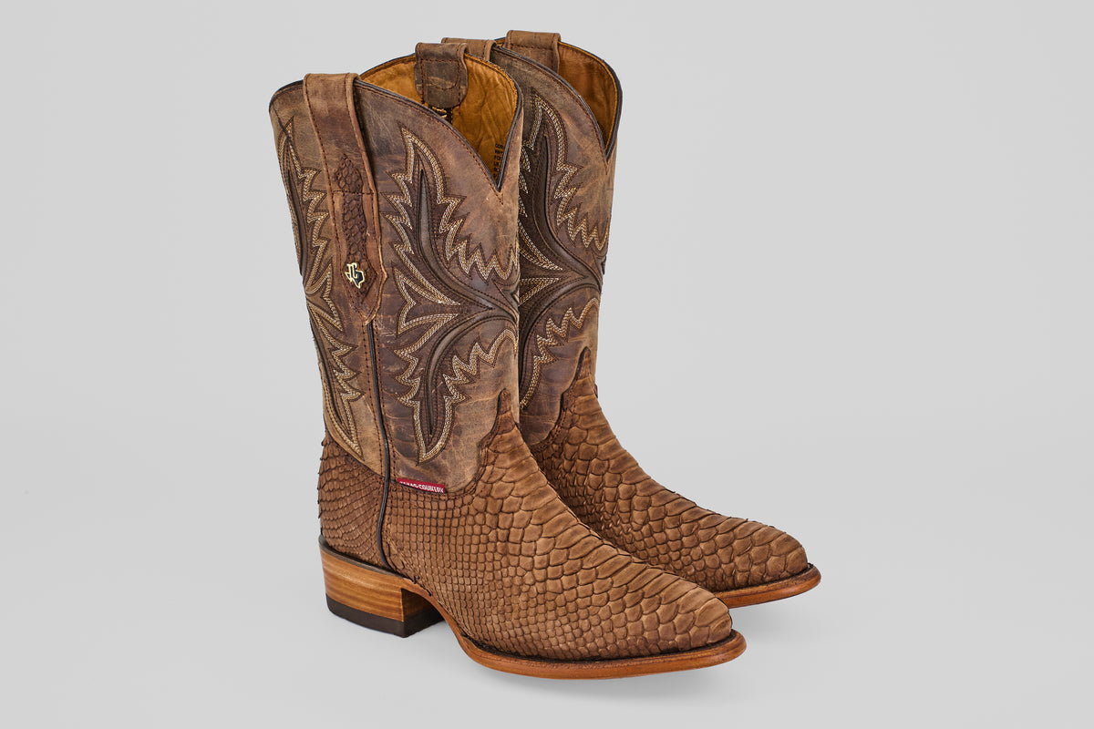 A pair of Tanner - Tamarindo - Round Toe cowboy boots in brown python leather, featuring intricate shaft stitching and a wooden heel, are positioned side by side on a light gray background.