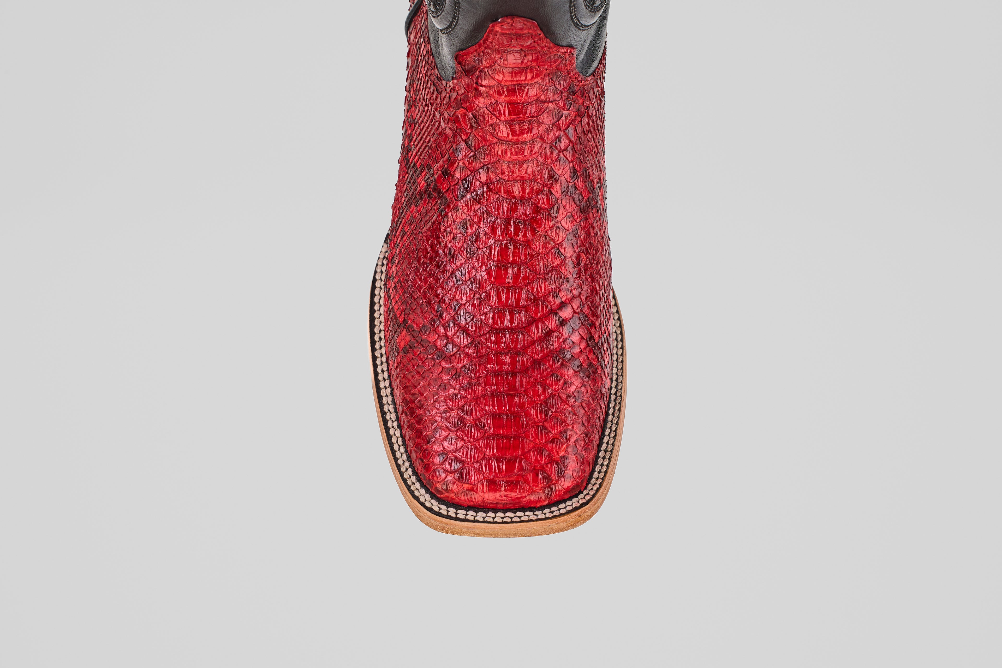 A close-up, top-down view of the Tanner - Ruby - Square Toe cowboy boot highlights its bold red snakeskin, square toe, and decorative stitching along the edge.