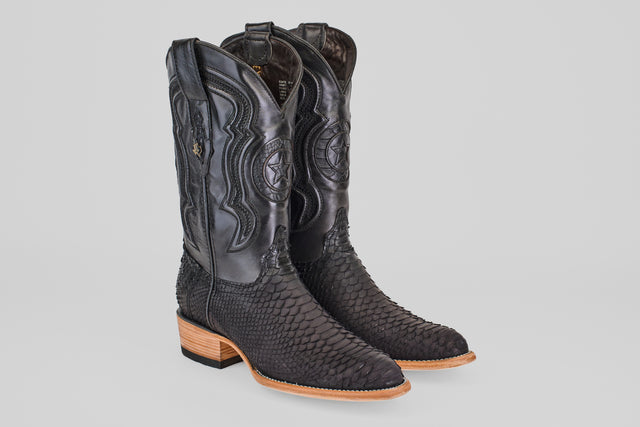 The Tanner – Matte Black – Roper Toe boots feature black, textured snakeskin-like leather, intricate shaft stitching, and light brown wooden heels and soles, shown against a plain gray background.