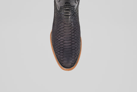 A top-down view of the Tanner – Matte Black – Roper Toe boot, featuring matte black python leather and a light brown sole, displayed on a plain white background.