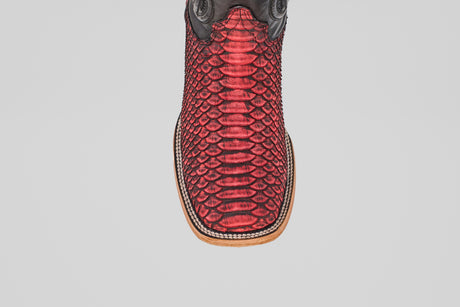 A close-up of the Tanner – Scarlet – Square Toe boot highlights its red python leather, black accents, and square light brown sole, capturing classic western style against a plain white background.