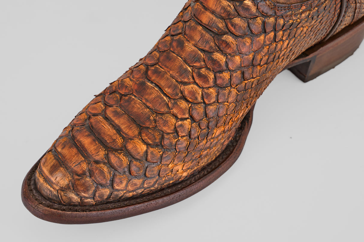 Close-up of the round toe of the Tanner – Chestnut boot, crafted from textured python leather with detailed scales and a sturdy wooden sole—a striking choice for western fashion enthusiasts.