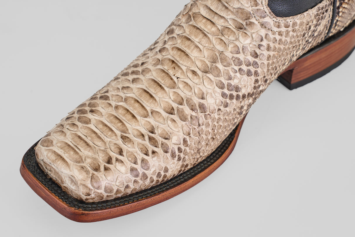 A close-up of the Tanner - Natural - Rodeo Toe boot shows its Python Natural snakeskin, visible scales, dark trim, and wooden sole—an ideal choice for a standout rodeo look.