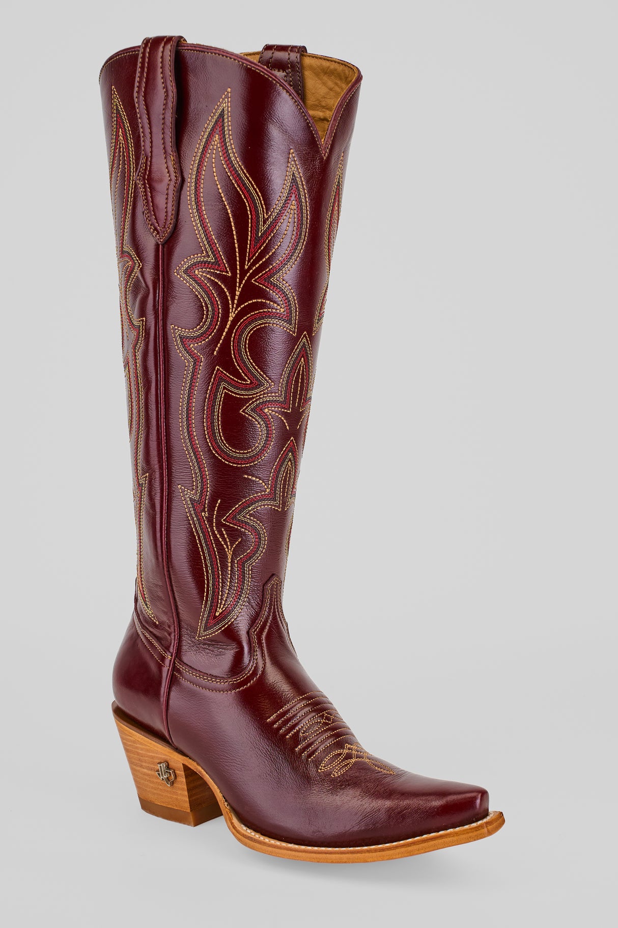 The Allison Blackberry - Tall Shaft - Snip Toe boot, in burgundy leather with decorative stitching, a pointed toe, and a medium wooden heel, is displayed against a plain light gray background.