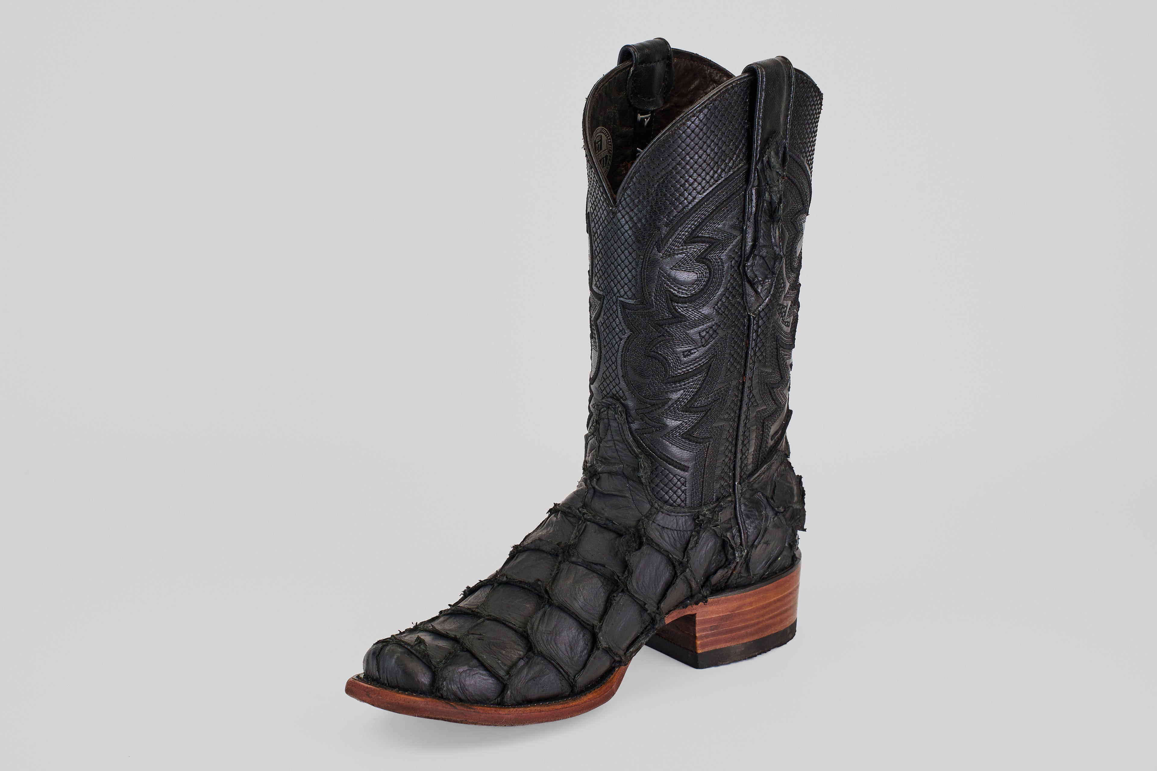 The Conor - Matte Black - Narrow Square Toe boot features a textured, scale-like pattern, decorative stitching on the shaft, and a brown wooden heel and sole. Photographed against a plain light gray background.