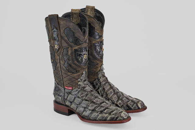 The Conor - Charcoal - Roper Toe is a pair of high men’s cowboy boots made from textured, scaly fish leather with intricate dark stitching and brown soles, shown on a plain light gray background.