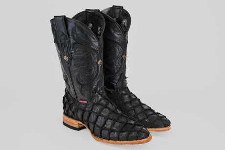 The Conor - Matte Black - Roper Toe boots feature textured pirarucu fish leather, high-calf design, decorative stitching, and light brown wooden heels, all showcased against a plain gray background.