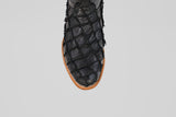 A close-up of the Conor - Matte Black - Roper Toe boot, featuring textured black pirarucu fish leather with a scale-like pattern and a brown sole, set against a plain light gray background.