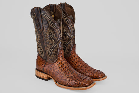 The Hornback Brown - Embossed Leather - Square Toe (E427) boots showcase intricate stitching on tall, dark brown shafts with light stacked heels and soles, all displayed against a plain gray background for a true Western style appeal.