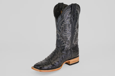 The Ostrich Black - Embossed Leather - Square Toe (E424) cowboy boot features decorative stitching, a high shaft, square toe, and tan stacked leather heel and sole. The textured black leather contrasts against a light gray background.