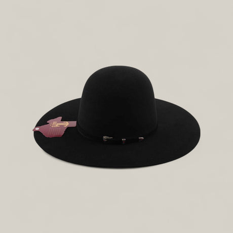 The 10X - Black - TC Hats features a wide brim, rounded crown, elegant decorative band, and a pink tag on the brim, shown against a plain beige background.