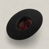 A 10X - Black - TC Hats open crown Texana hat is showcased upside down, displaying its maroon paisley satin lining against a plain light beige background.