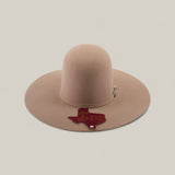 A 4x - Natural - TC Hats, a light brown, wide-brimmed felt Western hat with a decorative crown band, is shown on a plain background. A Texas-shaped tag reading TX HAT hangs from the brim.