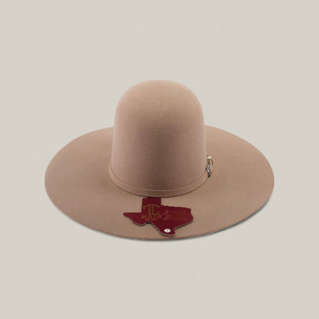 A 4x - Natural - TC Hats, a light brown, wide-brimmed felt Western hat with a decorative crown band, is shown on a plain background. A Texas-shaped tag reading TX HAT hangs from the brim.