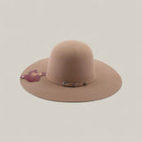The 4x - Natural - TC Hats is a wide-brimmed, light brown felt Western hat with an open crown, a small decorative band, and a maroon tag on the brim, shown against a plain, light background.