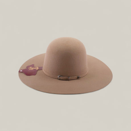 The 4x - Natural - TC Hats is a wide-brimmed, light brown felt Western hat with an open crown, a small decorative band, and a maroon tag on the brim, shown against a plain, light background.