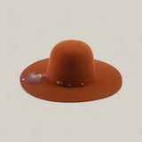 The 4x - Brick - TC Hats features a rust color, open crown, wide brim, rounded crown, decorative metal buckle, purple and gold side tag, and a stylish band, set against a plain beige background.