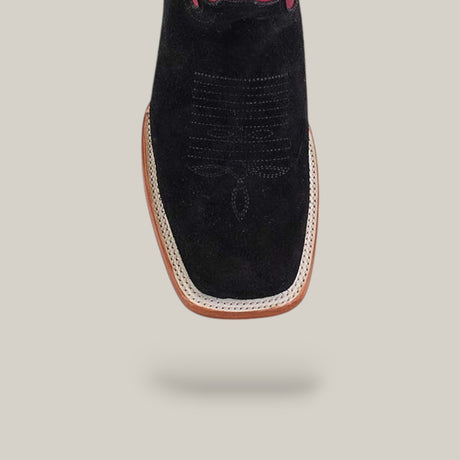 The Colt - Black - Square Toe boots are displayed from above on a beige background, featuring white stitching, tan trim, pink accents, and a premium suede finish that showcases their unique design details.