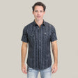 A man with short dark hair wears the Mens Performance Western Short Sleeve Aztec Print Navy Shirt (PGW10646) and light blue jeans, standing facing forward against a plain light beige background.