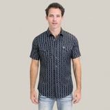 A man with short dark hair wears the Mens Performance Western Short Sleeve Aztec Print Navy Shirt (PGW10646) and light blue jeans, standing facing forward against a plain light beige background.