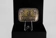 The Texas Country Buckle - Mod 1 is a decorative rectangular Western belt buckle with gold and silver floral designs, engraved with Texas Country Buckles, shown upright on a clear stand against a black background.