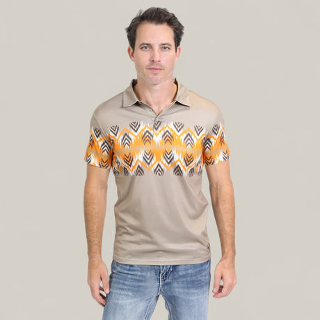 A man stands against a plain light gray background, wearing the Mens Performance Fabric Aztec Panoramic Print Khaki Polo (PGP10607) with a yellow and black geometric design across the chest and sleeves, paired with blue jeans.