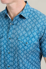 A man wears the Mens Performance Western Short Sleeve Aztec Print Blue Shirt (PGW10632) with a white geometric pattern, snap buttons, collar, and two chest pockets. Only his lower face and upper torso are visible.