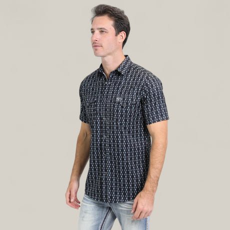 A man wearing the Mens Performance Western Short Sleeve Aztec Print Navy Shirt (PGW10646) and light blue jeans stands against a plain, light beige background.