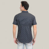 A man is standing with his back to the camera, wearing the Mens Performance Western Short Sleeve Aztec Print Navy Shirt (PGW10646) and light blue jeans against a plain light gray background.