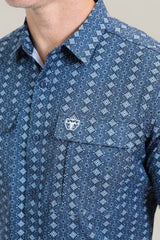 A man wears the Mens Performance Western Short Sleeve Aztec Print Navy Shirt (PGS10659), showcasing its geometric Aztec design and chest pocket with a white embroidered logo. Only his lower face and upper torso are visible.