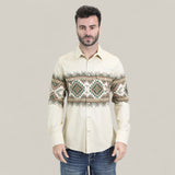 A man with short dark hair and a beard wears the Mens Western Modern Fit Cotton/Spandex Long Sleeve Beige Shirt with Snaps (WPL10677), featuring geometric patterns, paired with blue jeans. The background is plain light beige.
