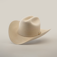 The 6X Real Belly, a light beige fur felt hat with a wide brim and decorative band, rests on a smooth white surface. Its premium Western design features a high crown with two slight dents that enhance its classic style.