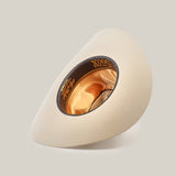 The 500X Superior Belly, a cream-colored cowboy hat made from 100% belly beaver fur, is displayed upside down to show off its satin-lined interior. A black band with gold lettering adorns the inside edge. The luxurious Western accessory contrasts against a plain white background.