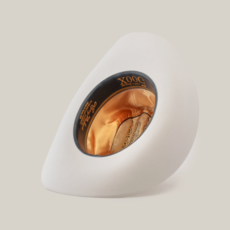 The 500X Superior White cowboy hat, made from premium belly beaver fur, is displayed on its side. Its interior features intricate gold embroidery and branding within the crown, set against a plain light-colored background.