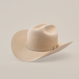 The 10X Jerarca Belly is a cream-colored cowboy hat made from luxurious fur felt, featuring a wide brim and distinctive crown crease. Adorned with a decorative metallic embellished band, this classic western headwear evokes Larry Mahans timeless style against a white backdrop.